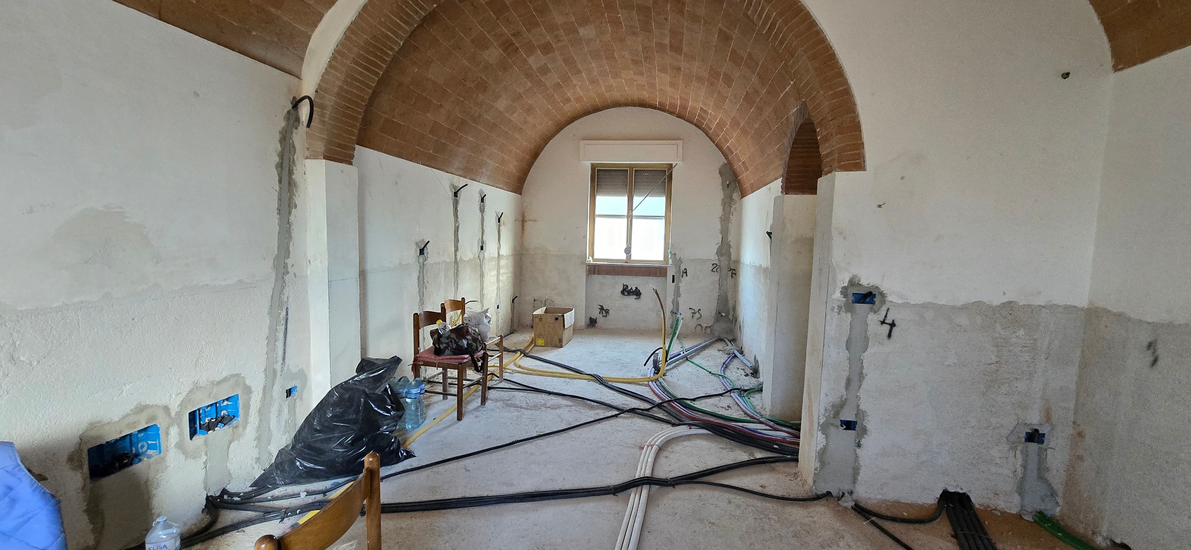Interni di una casa colonica in fase di ristrutturazione a Pisa: vista del cantiere con soffitto a volta in mattoni faccia a vista, nuovi impianti tecnologici e tracce alle pareti.