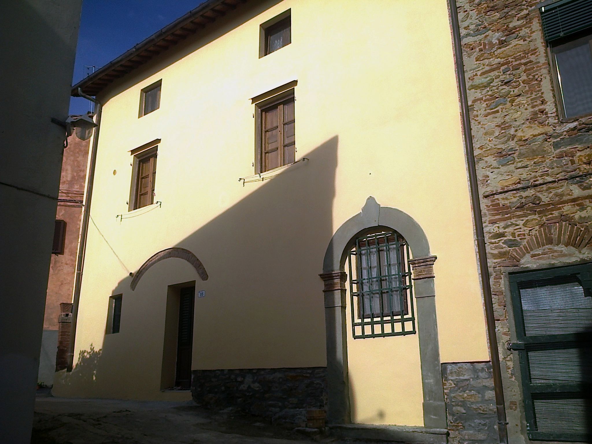 Facciata di una casa rustica toscana di colore giallo chiaro con infissi marroni. Ristrutturata da Edilvos