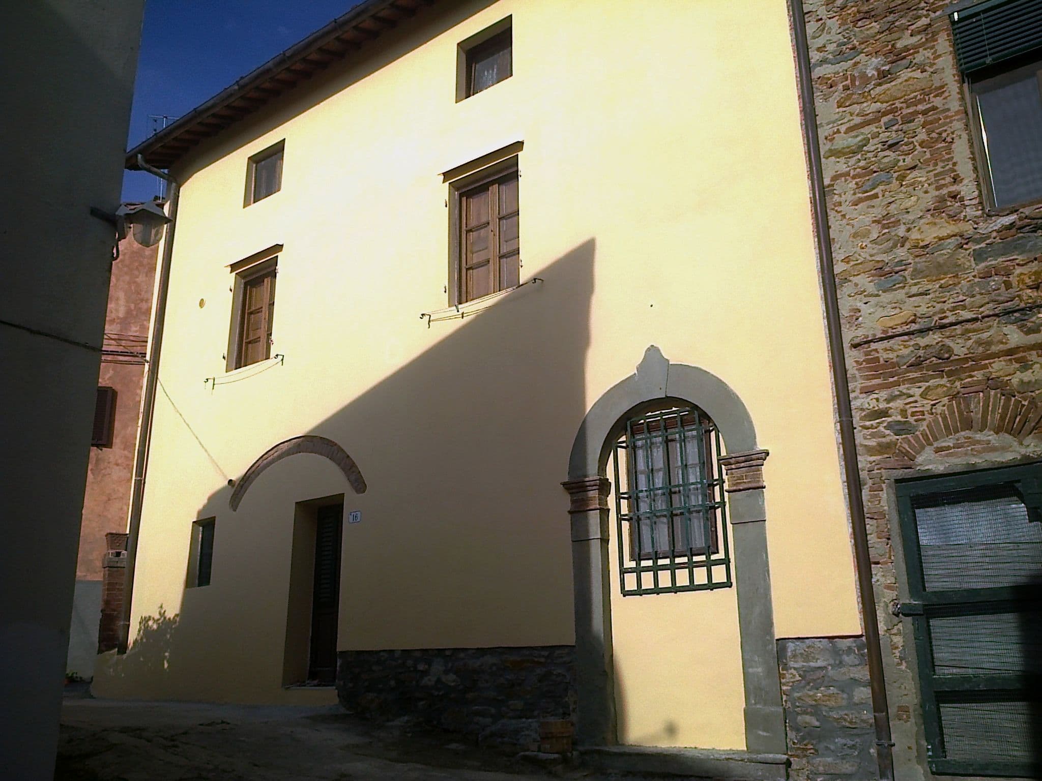 Facciata di una casa rustica toscana di colore giallo chiaro con infissi marroni. Ristrutturata da Edilvos